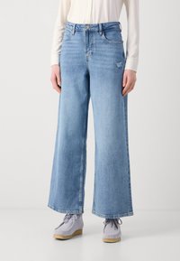 Lichtblauwe wijde jeans gemaakt van denim, met een lichte textuur en een subtiele beschadiging op het voorzakgebied.