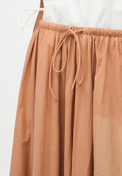 Φούστα ανοιχτό καφέ με ελαστική μέση και κορδόνι που δένει, συνδυασμένη με λευκή μπλούζα.