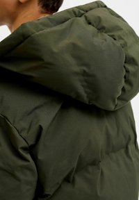 Giacca imbottita verde oliva con cappuccio, caratterizzata da un design trapuntato e una texture morbida, che presenta un'imbottitura spessa e una finitura liscia.