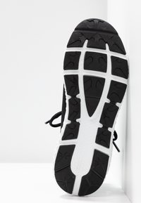 Black athletic shoe sole with prominent rubber tread patterns, featuring a white midsole and textured grip areas for traction.