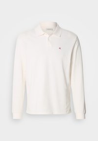 Kokvilnas krēmkrāsas polos krekls ar garām piedurknēm, kreisajā krūtīs ir izšūts sarkans logotips, klasisks apkakles dizains.