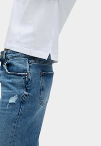 Weißes Baumwoll-T-Shirt mit abgerundetem Saum, kombiniert mit blauen Jeans aus Denim mit ausgefransten Details und kupferfarbenen Nieten.