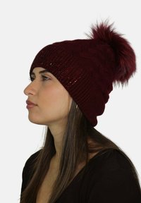 Berretto a maglia color marrone con motivo a treccia, dettagli scintillanti e pon pon in ecopelliccia sulla cima. Tessuto morbido, stile aderente.