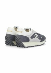 Zapatillas gris y blancas con materiales de ante y sintéticos, cuentan con una suela de goma texturizada, forma redondeada y una marca minimalista en el talón.