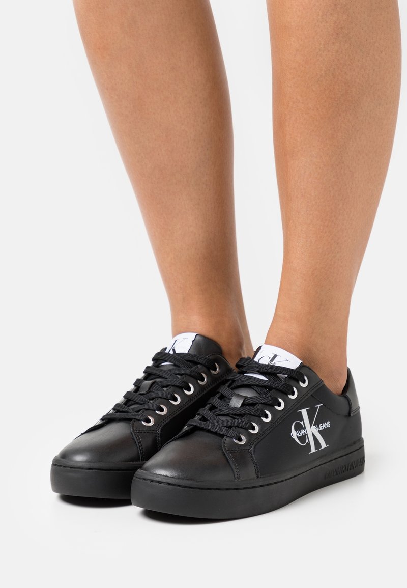 Czarne skórzane trampki z okrągłym noskiem, sznurówką, logo po boku i czarną gumową podeszwą. Gładka faktura i minimalistyczny styl.