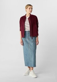 Burgunderfarbene Bomberjacke mit Reißverschluss, weiß und marineblau gestreiftes Oberteil, blaue Jeansmaxi-Rock und weiße Sneaker. Lässiges, geschichtetes Outfit.