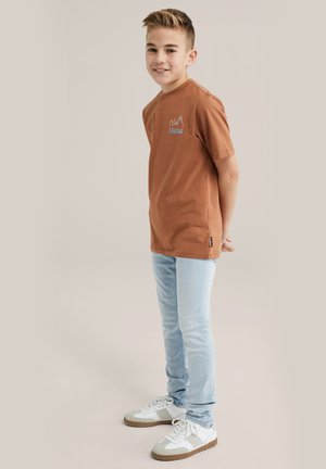 Bruine katoenen T-shirt met korte mouwen en een grafisch ontwerp. Lichtblauwe slim-fit jeans en witte sneakers met grijze accenten.