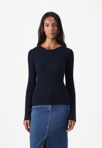 Pull-over en maille côtelée bleu marine à manches longues avec un col rond, associé à une jupe en denim avec une fente à l'avant, créant une silhouette ajustée.