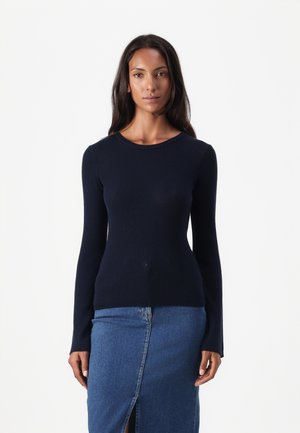 Pull-over en maille côtelée bleu marine à manches longues avec un col rond, associé à une jupe en denim avec une fente à l'avant, créant une silhouette ajustée.