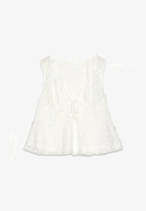 Blouse sans manches blanche avec un décolleté en V, ornée d'une broderie florale et d'un nœud à l'avant. Design évasé, texture de tissu douce.