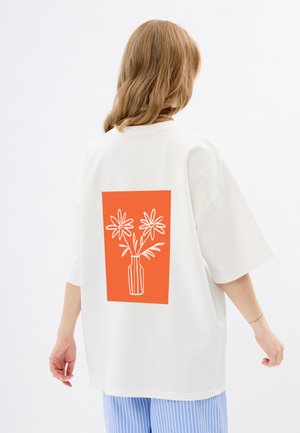 Weißes übergroßes T-Shirt mit einem großen orangefarbenen Rechteck auf dem Rücken, das eine weiße Strichzeichnung von Blumen in einer Vase zeigt. Kurze Ärmel.