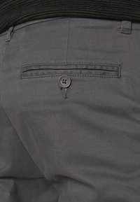 Pantaloni grigi con una texture liscia, dotati di una tasca posteriore e una chiusura con bottone nero, con cuciture dettagliate lungo il bordo della tasca.