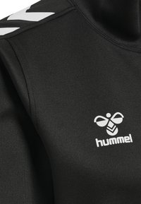 Zwart sportshirt gemaakt van gladde stof, met een wit logo en chevronontwerp op de schouder. Ronde halslijn, aansluitende pasvorm.