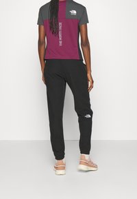 T-shirt med kort ärm i grått och vinrött med logotyp; tillsammans med svarta joggingbyxor med logotyp på benet.