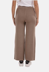 Pantaloni a gamba larga in maglia marroni con vita alta, texture liscia e vestibilità comoda, abbinati a sneakers bianche con dettagli neri.