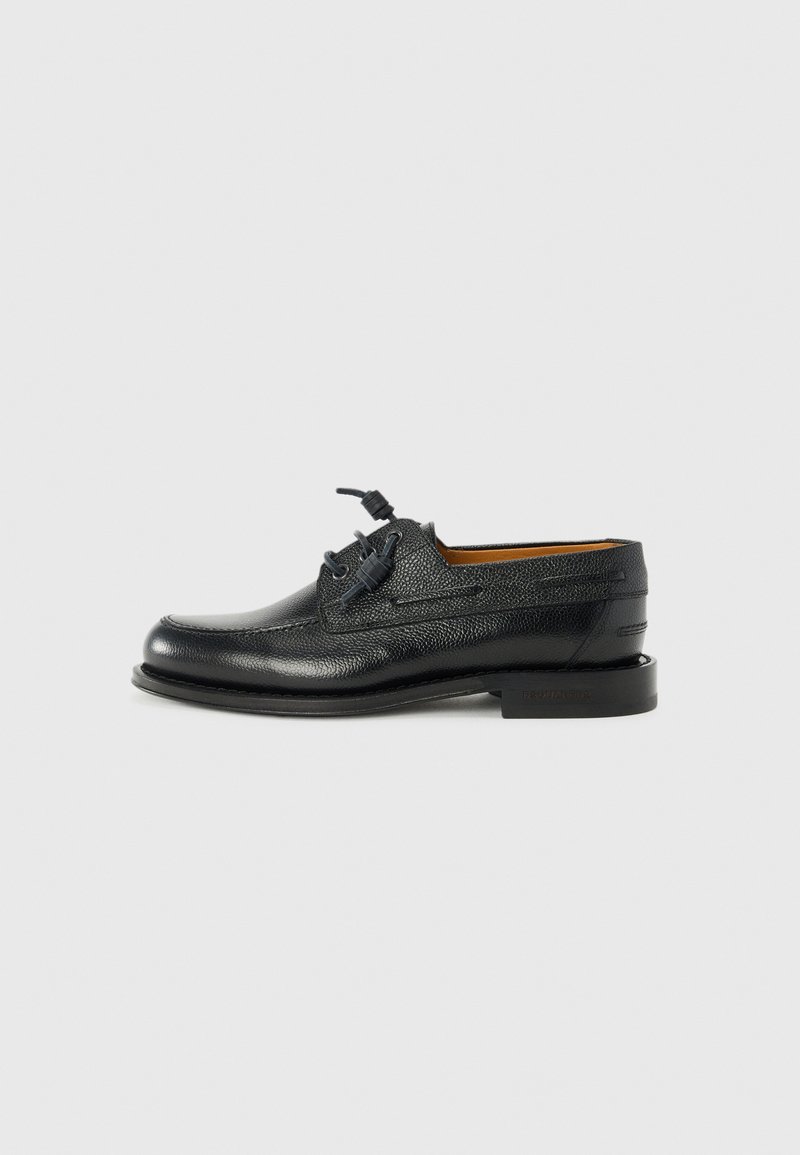 Chaussures habillées en cuir noir avec une finition texturée, ornées de lacets ronds, d'un design épuré et d'une semelle à profil bas.