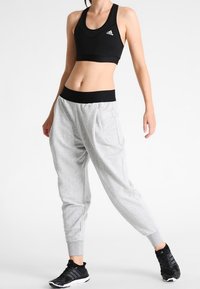 Zwart sport-bh, grijze tapered sweatpants met manchetten bij de enkels, met een zwarte tailleband. Zwarte sneakers ronden de outfit af.