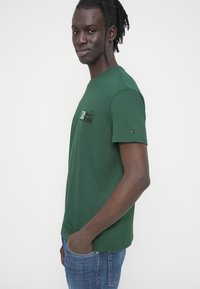 Πράσινο βαμβακερό μπλουζάκι με κοντά μανίκια, με κεντημένο λογότυπο στο στήθος και μικρή λεπτομέρεια λογότυπου στο μανίκι.