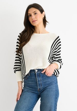 Schwarz-weißer gestreifter Strickpullover mit herabgesetzten Schultern, lockerem Schnitt und gerippten Bündchen, kombiniert mit hoch taillierten blauen Jeans. Texturiert.