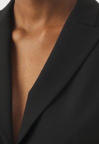 Black blazer with a notched collar; smooth fabric texture; close-up view of neckline and upper chest. No visible patterns or hardware.