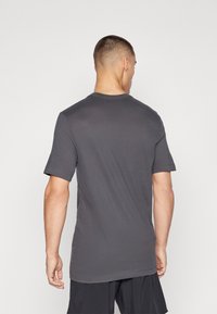 Grå kortermet T-skjorte vist bakfra, laget av glatt stoff med rund hals og lett buet nedre kant. Minimalistisk design, ingen mønstre.