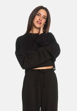Felpa nera corta con maniche ampie e texture morbida, abbinata a pantaloni sportivi dalla vestibilità rilassata con vita elasticizzata e coulisse.