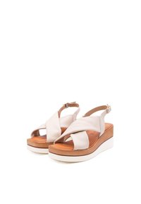 Sandali con zeppa in morbida pelle beige, con un design a incrocio, dotati di una suola platform marrone e cinturino alla caviglia regolabile.