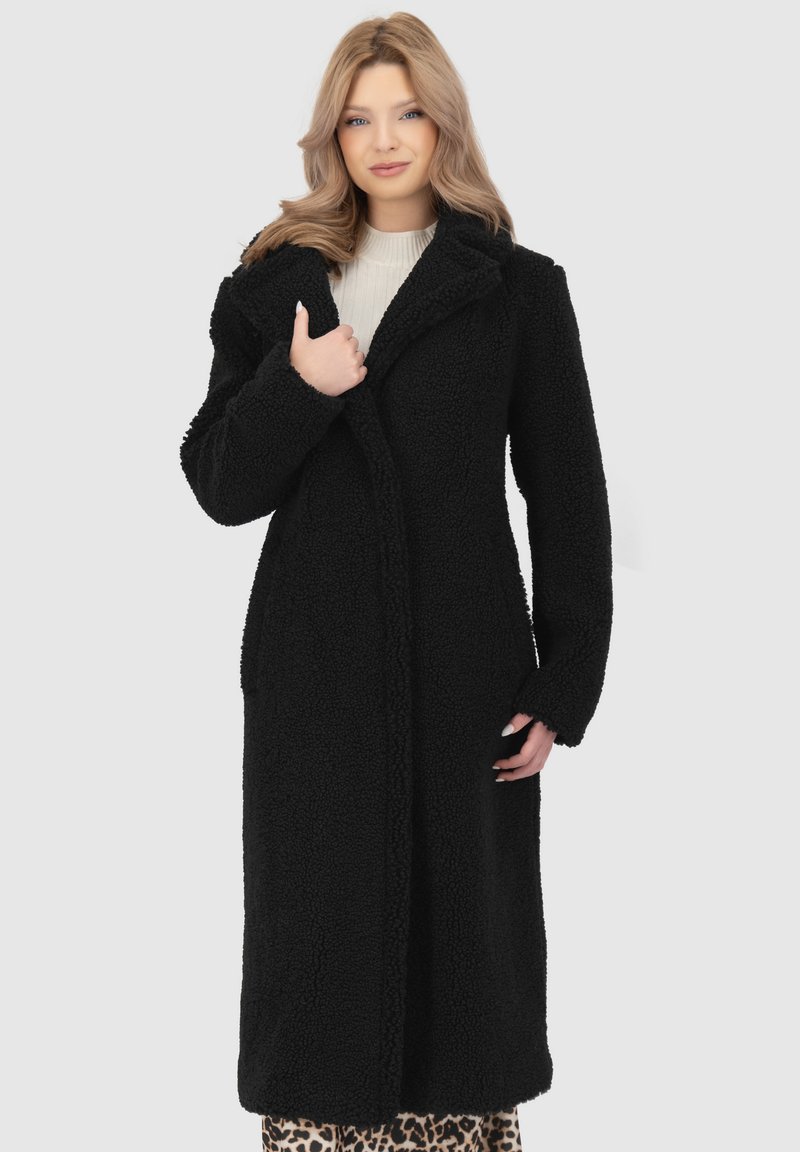 Cappotto lungo nero in tessuto testurizzato, con colletto e apertura davanti. Le maniche sono leggermente oversize, conferendo un aspetto accogliente.