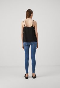 Top nero senza maniche con un design fluido, abbinato a jeans blu aderenti. Texture liscia e stile minimalista. Sandali semplici completano il look.