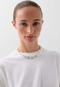 Collana in argento con anelli ovali intrecciati, indossata sopra una camicia bianca a collo rotondo, texture liscia e design minimal.
