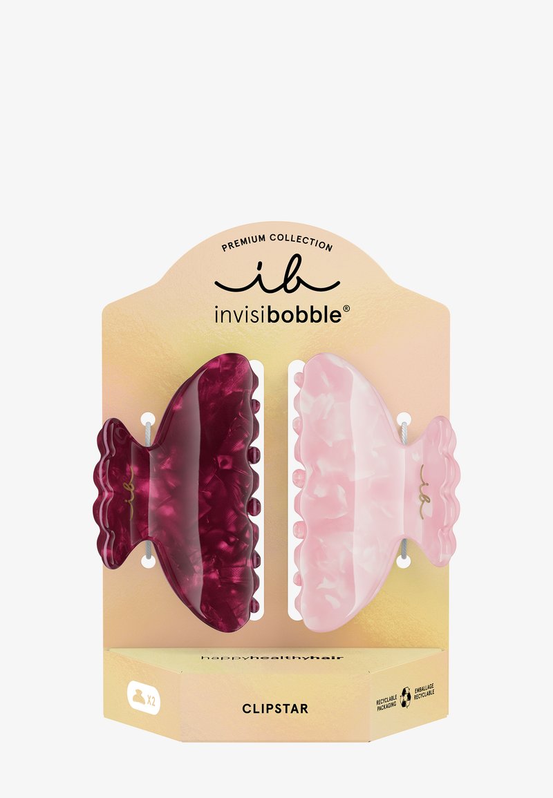 Deux pinces à cheveux marbrées, une rouge profond et une rose clair, présentées dans un emballage doré portant l’étiquette "invisibobble Clipstar" avec des icônes recyclables.