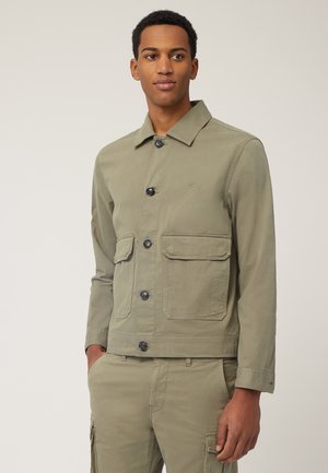 Olive green, long-sleeve jacket with a collared neck, front button closure, and two patch pockets on the chest. Smooth cotton blend fabric.