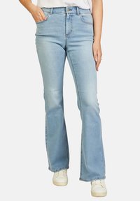 Lichtblauwe flared jeans van denim, met een hoge taille, voorzakken en een subtiele vervaging, gecombineerd met witte sneakers.