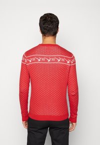 Maglione rosso con motivi di renne bianche e fiocchi di neve, tessuto lavorato a maglia, scollatura rotonda e polsini e orlo a coste. Vista posteriore.