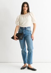 Blusa bianca a pois con maniche a sbuffo, jeans blu a vita alta e una pochette nera intrecciata. Ballerine nere completano l'outfit.
