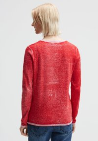 Roter Pullover mit langen Ärmeln und einer strukturierten, leicht verblassten Oberfläche. Verfügt über einen runden Halsauschnitt und kontrastierende gerippte Bündchen und Saum.