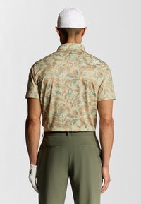 Kortärmad skjorta i ljus persika med ett blommigt mönster, matchad med olivgröna byxor. Tyget verkar andas och har en subtil textur.