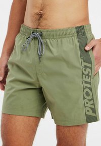 Olijfgroene zwemshorts met een zwart gestreepte logoprint, elastische tailleband en zwart-wit trekkoord. Glad, lichtgewicht materiaal.