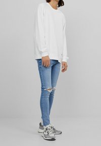 Sudadera blanca, puños acanalados, corte relajado, combinada con vaqueros claros rasgados y zapatillas gris y blancas con detalles de malla.