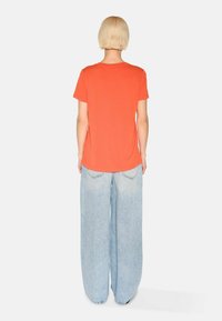 Short-sleeve, bright orange t-shirt with a relaxed fit, paired with wide-leg light blue jeans, showcasing a smooth texture and simple design.