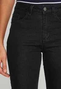 Jeans en denim noir au design slim, avec cinq poches et un bouton en métal argenté. Le tissu a une texture lisse avec un léger stretch.