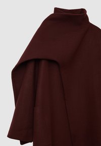 Burgunderfarbener Wollponcho mit hohem Kragen, oversized drapierter Form und einer seitlichen Tasche; texturiertes Material mit subtilen Webmuster.