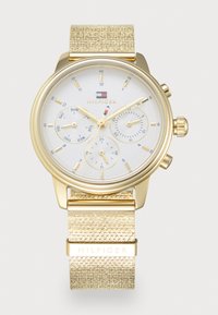 Goldfarbene Uhr mit einem strukturierten goldenen Armband, weißem Zifferblatt mit drei Unterzifferblättern und einem Markenlogo an der oberen Mitte.