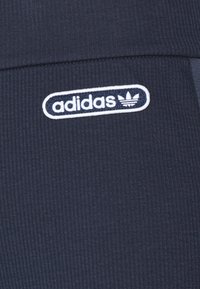 Adidas-logotyp i vit brodering på mörkblå ribbad tyg av ett plagg.