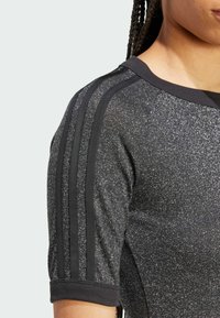 Czarna sportowa koszulka z teksturowaną, błyszczącą powierzchnią, z prążkowanym kołnierzykiem i rękawami oraz trzema czarnymi paskami na ramionach.