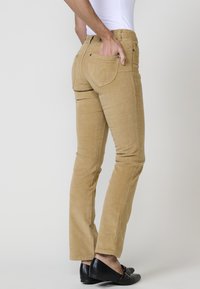 Tant corduroy broek met een slim fit, voorzien van achterzakken met decoratieve stiksels en een ritssluiting, gecombineerd met zwarte loafers.