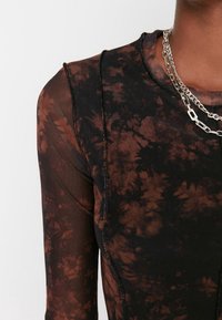 Top a maniche lunghe tie-dye nero e marrone, con texture trasparente, vestibilità aderente e cuciture a contrasto, accessoriato con catene d'argento sovrapposte.