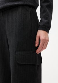 Pantalons noirs à rayures, fabriqués en tissu texturé avec une poche latérale et une coupe décontractée, présentant des coutures visibles et une taille confortable.