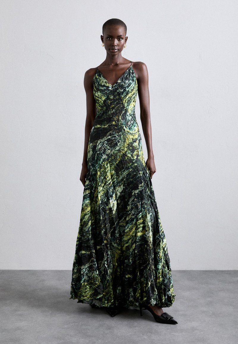 Vestido maxi con un patrón ondulado en negro, verde y amarillo. Tiene tirantes finos y una falda fluida y texturizada que cae con elegancia.