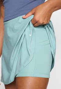 Falda de tenis en un verde azulado claro con un diseño flexible. Presenta un logo de Nike, textura suave y tejido en capas para facilitar el movimiento.